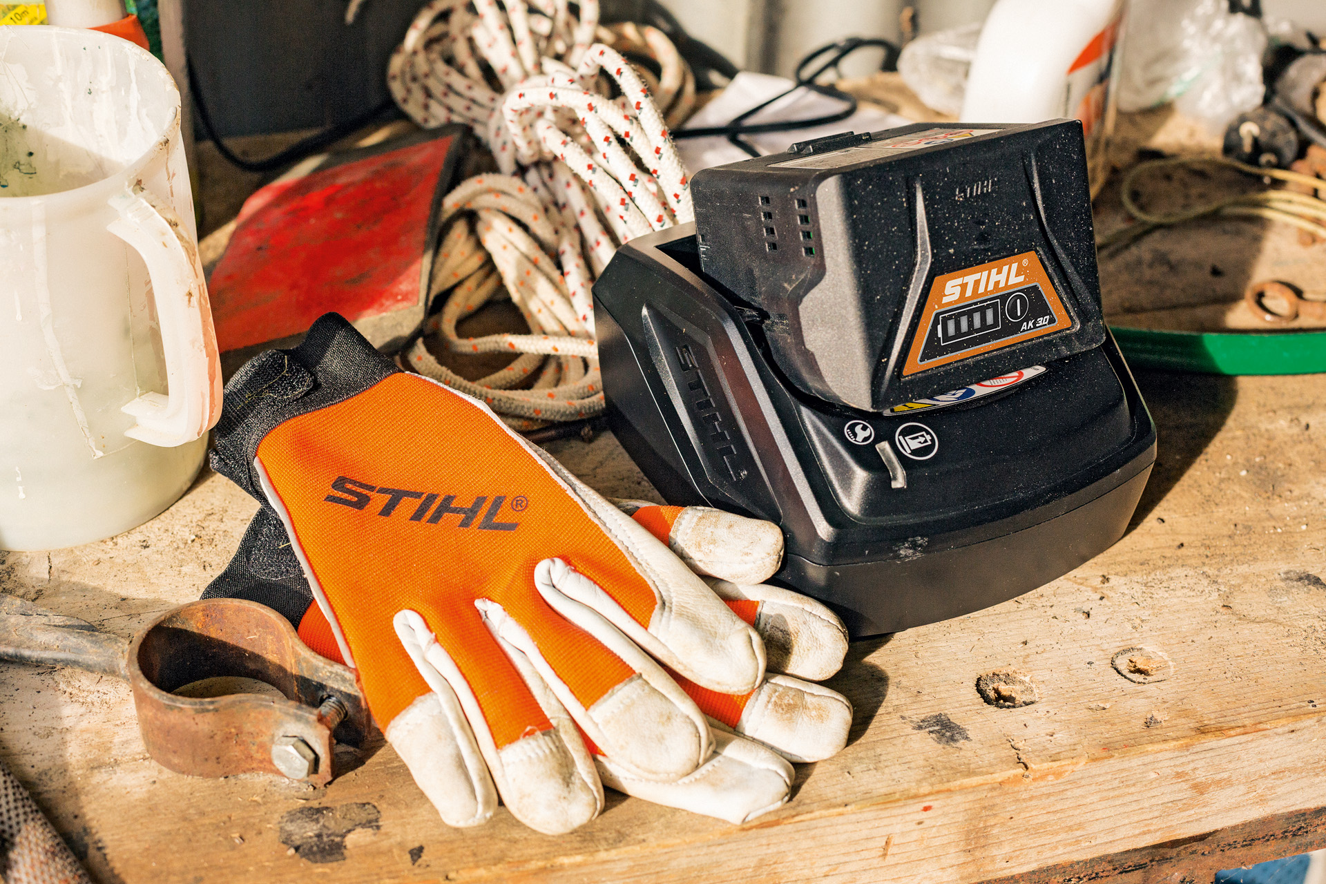 Unas baterías de iones de litio de la serie AK se están cargando junto a unos guantes y unas herramientas de trabajo STIHL