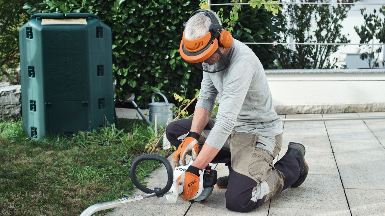 Una persona, equipada con ropa de protección, presiona la desbrozadora de gasolina STIHL FS 38 sobre el suelo