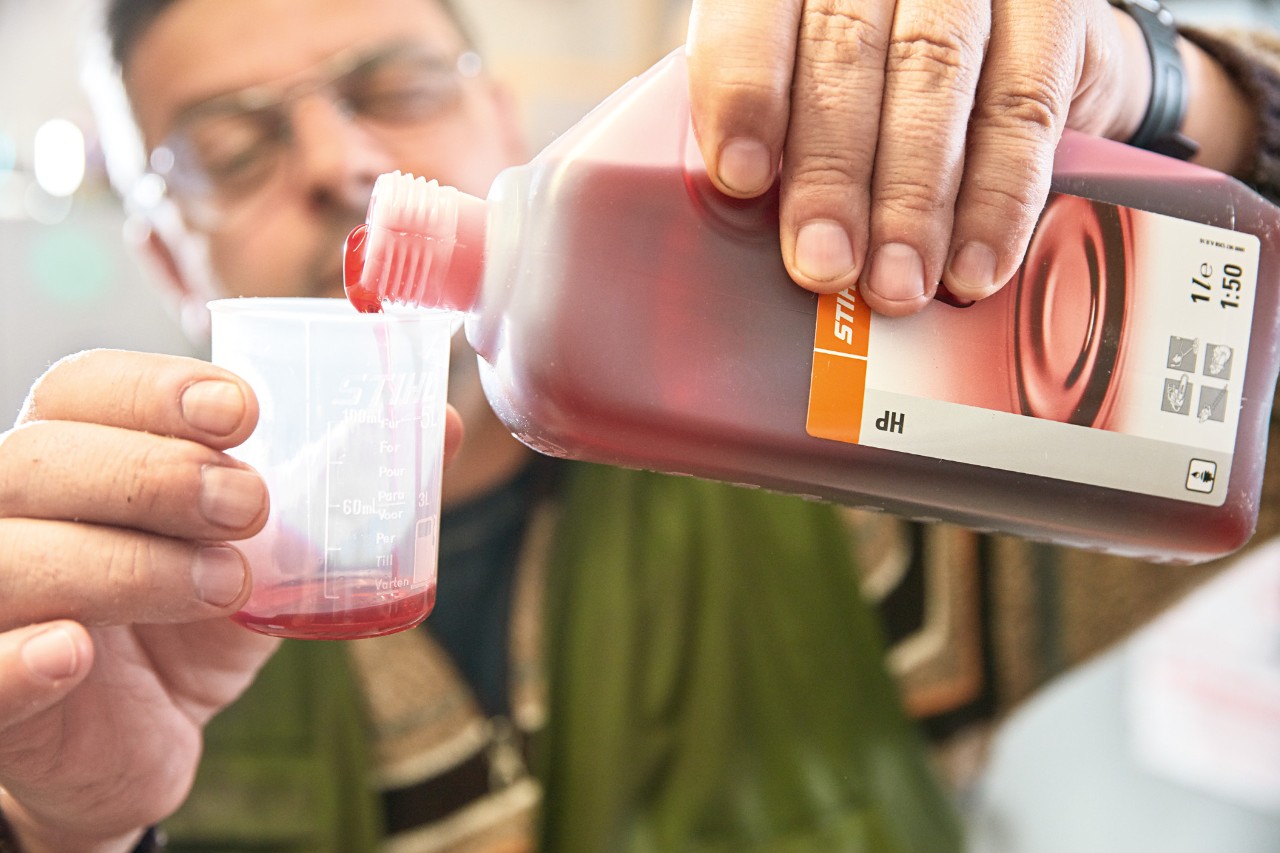 Un hombre vierte aceite de motor de 2 tiempos STIHL HP en un vaso de medición