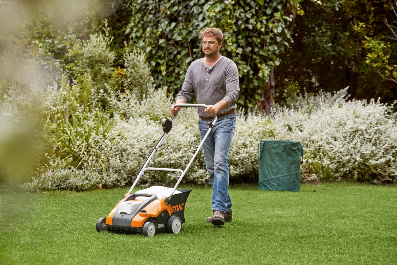 Un hombre escarifica el césped verde con un escarificador de batería STIHL RLA 240