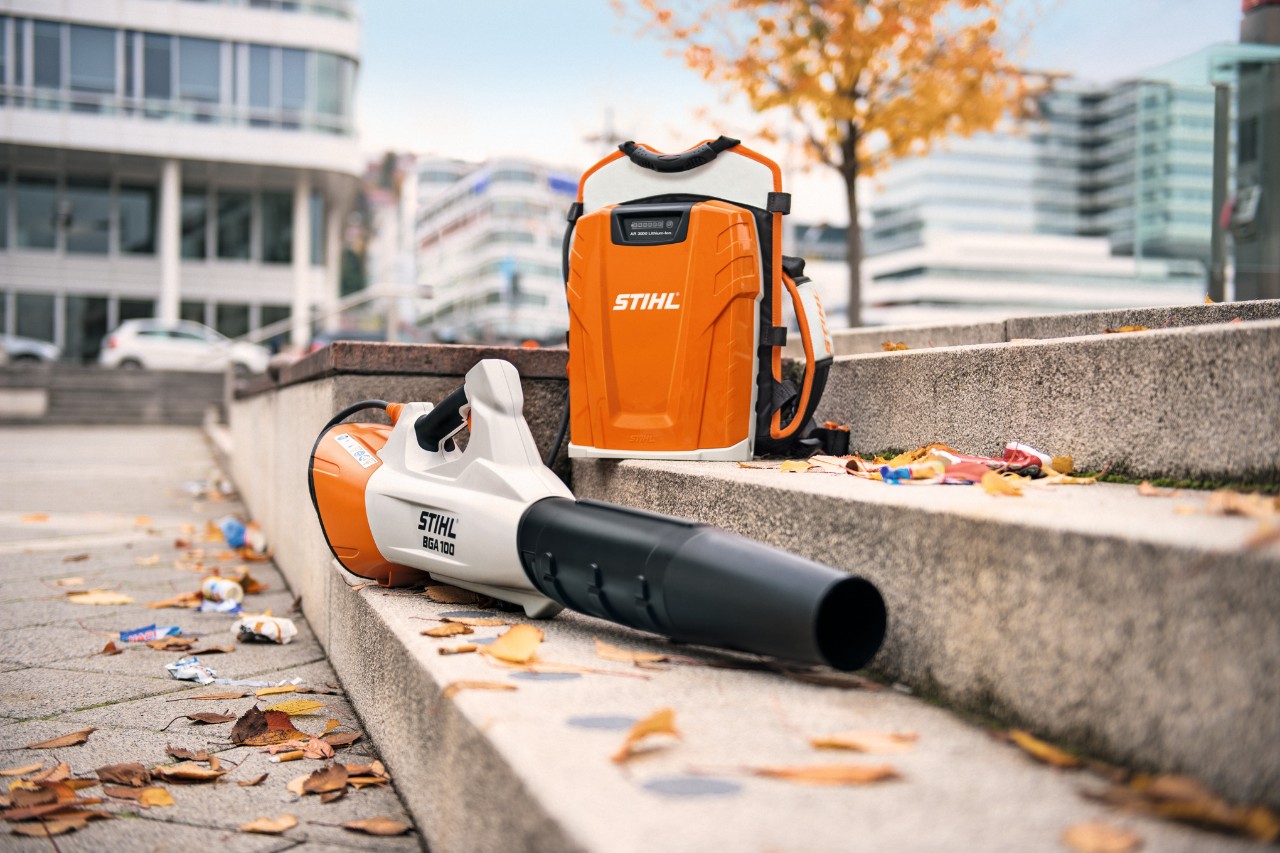 El soplador de batería STIHL BGA 100 y la batería profesional de mochila STIHL AR 3000 L están sobre una escalera de piedra con algunas hojas.