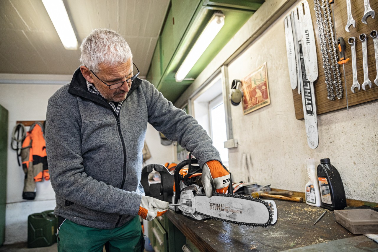 Un hombre en un taller atornilla una motosierra con la espada STIHL Rollomatic E 