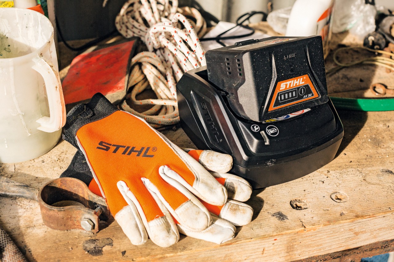 Sobre una superficie de trabajo reposan una batería y unos guantes