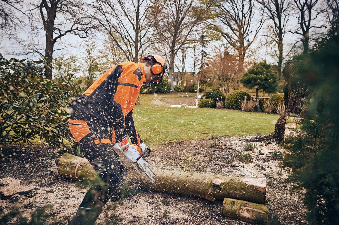 Un hombre con equipamiento de protección corta un tronco en una zona verde con una motosierra de batería STIHL